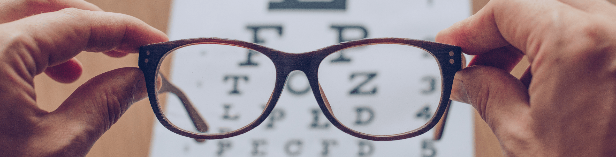 Close-up of hands holding a pair of eyeglasses in front of an eye chart.